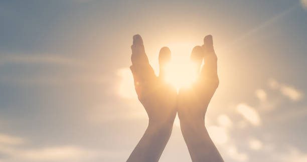 Praying hands silhouetted against the sun